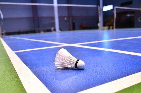 Nahaufnahme eines Federballs auf einem blauen Badmintonfeld mit weißen Linien.