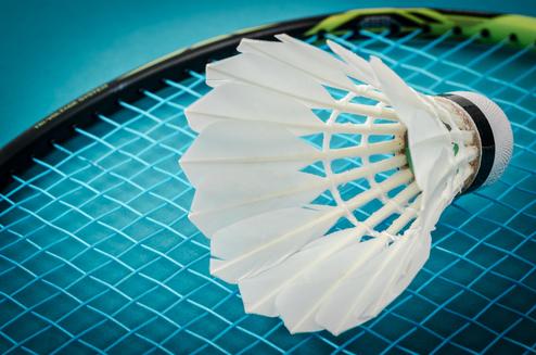 Nahaufnahme eines Federballs auf einem Badmintonschläger vor einem blauen Hintergrund.