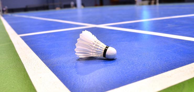 Nahaufnahme eines Federballs auf einem blauen Badmintonfeld mit weißen Linien.