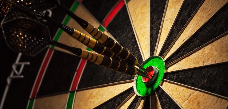 Drei Pfeile stecken im roten Bullseye einer Dartscheibe, umgeben von schwarzen und grünen Feldern.