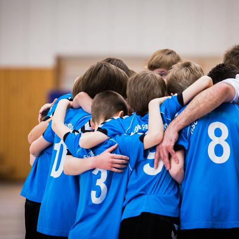 Gruppe junger Sportler in blauen Trikots umarmt sich in einer Halle vor dem Spiel.