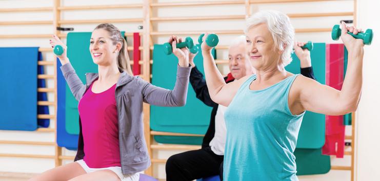 Drei Personen mit Hanteln sitzen auf großen Gymnastikbällen und trainieren in einem Fitnessraum.