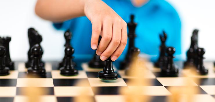 Hand eines Spielers bewegt eine schwarze Schachfigur auf einem Schachbrett mit schwarzen und weißen Feldern.