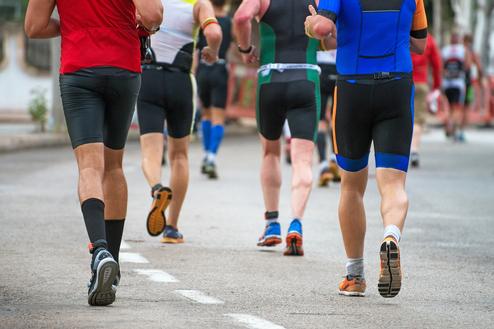 Gruppe von Männern in Sportkleidung joggt auf einer asphaltieren Straße, während sie dem Rennen folgen.