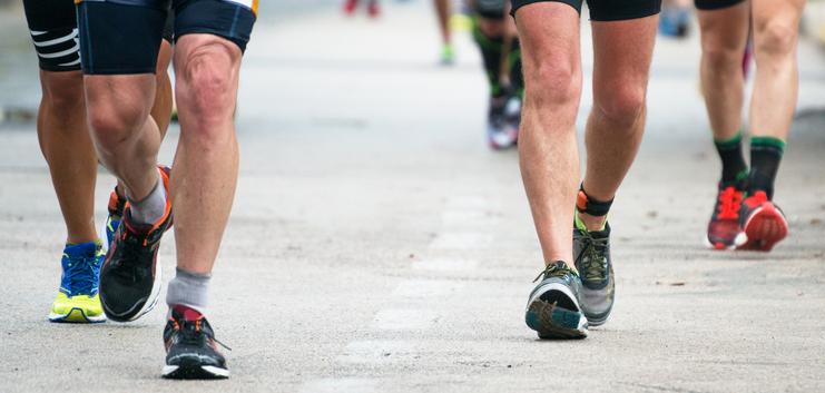 Beine von Läufern in Sportkleidung, die auf einer Asphaltstraße unterwegs sind. Ein Läufer trägt einen Zeitmesschip.