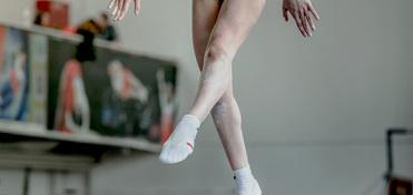 Athletisches Bein mit speziellen Turnschuhen schwebt über einem Schwebebalken in einer Trainingsumgebung.